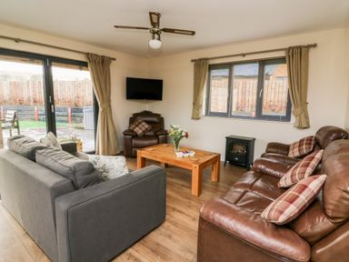 A living room with sofas wooden coffee table tv and patio doors at Caban Nant Ddu in Rhayader