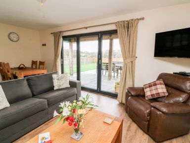 A living room with a sofa armchair coffee table and dining table near glass doors showing a patio at Caban Nant Ddu in Rhayader