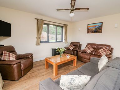 A living room with brown leather armchairs a gray fabric sofa a wooden coffee table with flowers and a window with curtains at Caban Nant Ddu in Rhayader