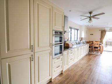 A kitchen with cream cabinets a dining table and chairs and wooden floor at Caban Nant Ddu in Rhayader