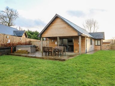 A wooden cabin with a patio table set and hot tub in a fenced backyard at Caban Nant Ddu in Rhayader