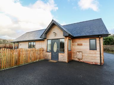 A wooden cabin with a gray door and a fenced yard at Caban Nant Ddu in Rhayader