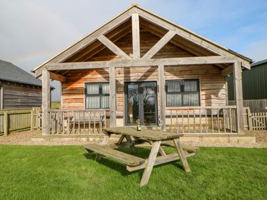 A wooden cabin with a covered porch and a picnic table on grass at Wansbeck in Longframlington near Alnwick