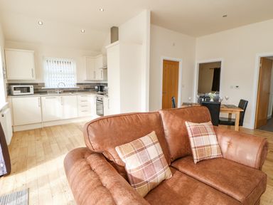 An open plan room with a brown sofa, a kitchen with white cabinets and a dining table with black chairs at Wansbeck in Longframlington near Alnwick