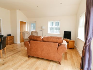 A living room with a brown sofa two armchairs a wooden TV stand with a television and wooden flooring at Wansbeck in Longframlington near Alnwick