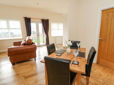A dining area with a wooden table set for four and a brown leather sofa near glass doors leading outside at Wansbeck in Longframlington near Alnwick