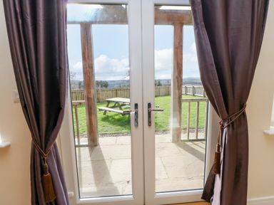 Double glass doors with purple curtains opening to a patio and garden with a picnic table at Wansbeck in Longframlington near Alnwick