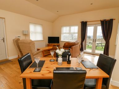 A dining table set with wine glasses and a bottle in a living room with sofas and a television at Wansbeck in Longframlington near Alnwick