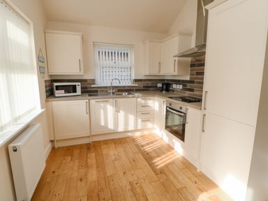 A kitchen with wooden floor white cabinets a microwave oven a kettle and a window at Wansbeck in Longframlington near Alnwick