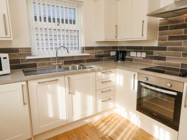 A kitchen with white cabinets a microwave a kettle a sink and an oven at Wansbeck Longframlington near Alnwick