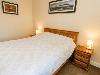 A bedroom with a wooden bed and two wooden bedside tables with lamps and framed pictures on the walls at Wansbeck in Longframlington near Alnwick