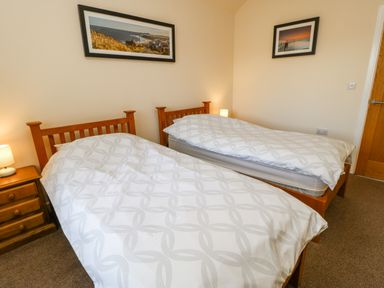 A bedroom with two single beds with patterned white bedding a wooden nightstand with a lamp and two framed pictures on the walls at Wansbeck in Longframlington near Alnwick
