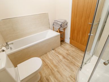 A bathroom with a bathtub a toilet a wooden door a shower and towels on a rack at Wansbeck in Longframlington near Alnwick