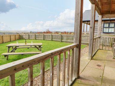 A wooden patio with railing overlooking a grassy fenced garden with a picnic table and bottle at Wansbeck in Longframlington near Alnwick