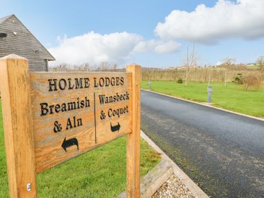 A wooden signpost directing to Holme Lodges with a road and grassy area in the background at Wansbeck in Longframlington near Alnwick