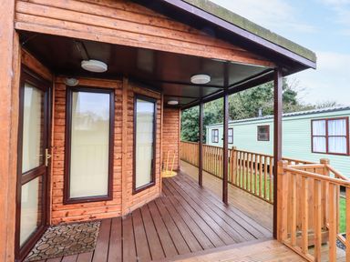 A wooden covered porch with railings and windows at Roe Deer Lodge in Castlewigg near Whithorn