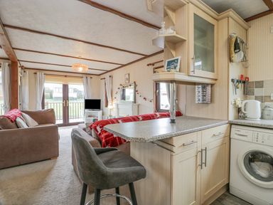 A living area with sofas and a television beside a kitchen counter with a bar stool at Roe Deer Lodge in Castlewigg near Whithorn