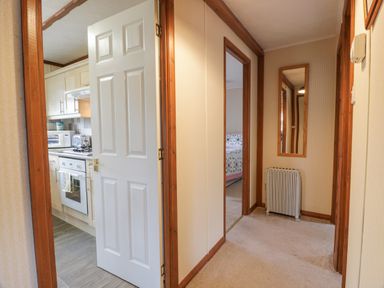 A hallway with a door open to a kitchen and an opening to a bedroom with a bed and quilt at Roe Deer Lodge Castlewigg near Whithorn