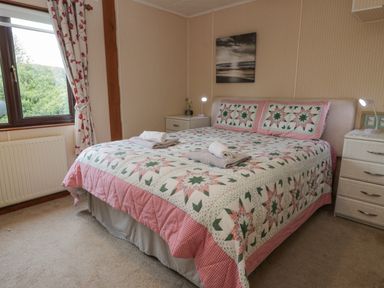 A bedroom with a double bed covered by a quilt with star patterns two bedside tables lamps and a window with floral curtains at Roe Deer Lodge Castlewigg near Whithorn