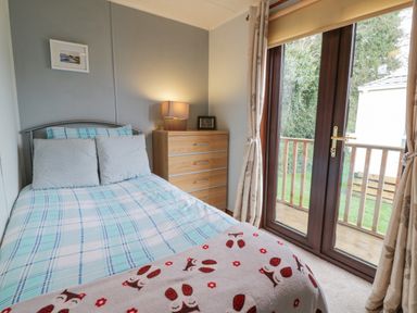 A bedroom with a bed, dresser, lamp, framed picture, and glass doors leading outside at Roe Deer Lodge in Castlewigg near Whithorn
