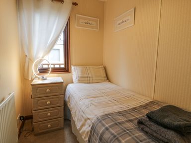 A small bedroom with a single bed next to a window and a bedside cabinet with a round lamp at Roe Deer Lodge Castlewigg near Whithorn