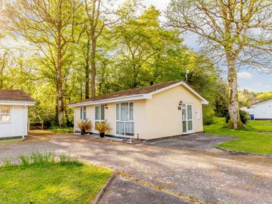 A single-story house with windows and doors surrounded by trees and grass at Brook Cottage Rosecraddoc Lodge near Liskeard
