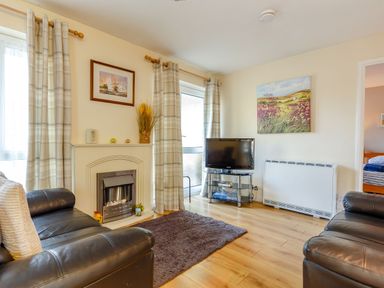 A living room with two black leather sofas a fireplace a TV on a stand and windows with curtains at Brook Cottage Rosecraddoc Lodge near Liskeard
