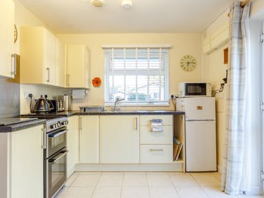 A kitchen with beige cabinets a black countertop a stove microwave refrigerator and a window with blinds at Brook Cottage in Rosecraddoc Lodge near Liskeard