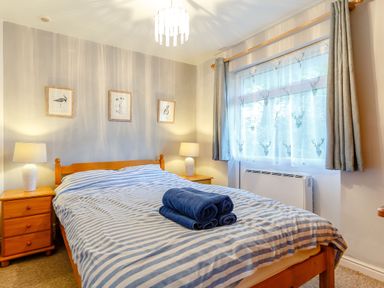 A bedroom with a wooden bed and striped bedspread with towels on top at Brook Cottage in Rosecraddoc Lodge near Liskeard