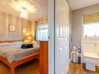A bedroom with a wooden bed and striped bedding next to a bathroom with a toilet and window at Brook Cottage Rosecraddoc Lodge near Liskeard