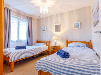 A bedroom with two single beds striped bedding and a bedside table with a lamp at Brook Cottage Rosecraddoc Lodge near Liskeard