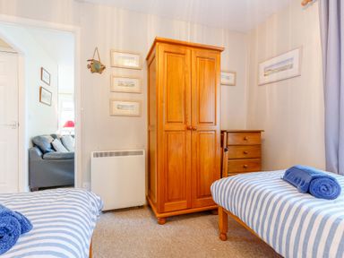 A bedroom with two single beds striped bedding wooden wardrobe and chest of drawers at Brook Cottage in Rosecraddoc Lodge near Liskeard