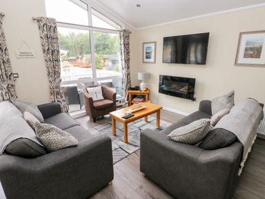 A living room with two sofas, an armchair, a coffee table, a wall-mounted TV and fireplace at 95 The Haven in Wisemans Bridge near Saundersfoot