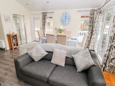 A living room with a dark grey sofa and dining table with six chairs and a clock on the wall at 95 The Haven in Wisemans Bridge near Saundersfoot