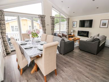 An open plan living room and dining area with a table set for six and sofas facing a wall-mounted TV at 95 The Haven Wisemans Bridge near Saundersfoot