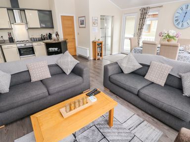 A living area with two gray sofas and a wooden coffee table next to a kitchen and dining area at 95 The Haven in Wisemans Bridge near Saundersfoot