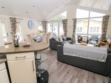 An open living and dining area with gray sofas dining table and large windows at 95 The Haven in Wisemans Bridge near Saundersfoot