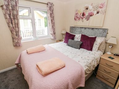 A bedroom with a bed with pillows and folded towels a bedside table with a lamp and a window with curtains at 95 The Haven Wisemans Bridge near Saundersfoot