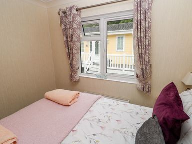 A bedroom with a bed floral bedding and two folded towels near a window with floral curtains at 95 The Haven Wisemans Bridge near Saundersfoot