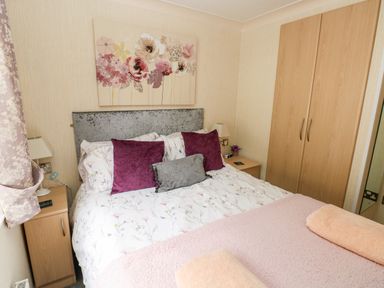 A bedroom with a bed with floral bedding and purple and gray pillows between two wooden bedside tables and a wardrobe at 95 The Haven Wisemans Bridge near Saundersfoot