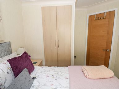 A bedroom with a bed with pillows and folded towels a wooden wardrobe and a wooden door at 95 The Haven in Wisemans Bridge near Saundersfoot