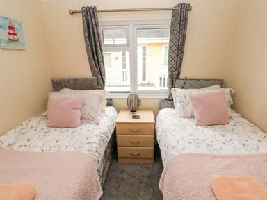 A bedroom with two single beds a wooden nightstand and a window with curtains at 95 The Haven in Wisemans Bridge near Saundersfoot