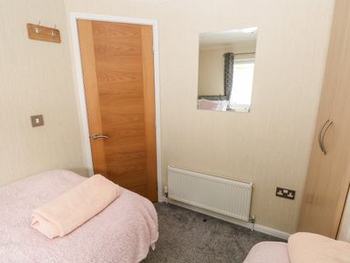 A small bedroom with a wooden door a bed covered with a pink blanket and towel a wall mirror a radiator and a wardrobe at 95 The Haven in Wisemans Bridge near Saundersfoot