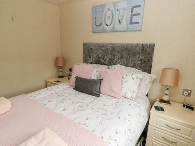 A bedroom with a bed with floral bedding and pillows between two bedside tables with lamps at 95 The Haven in Wisemans Bridge near Saundersfoot