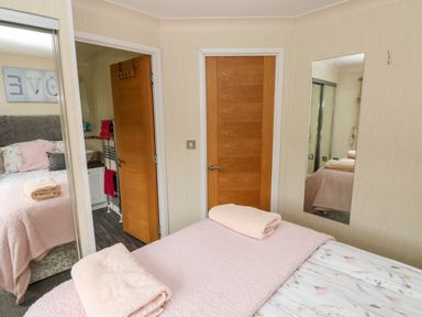 A bedroom with a bed covered in floral sheets and pink blankets and towels with two wooden doors and a wall mirror at 95 The Haven in Wisemans Bridge near Saundersfoot