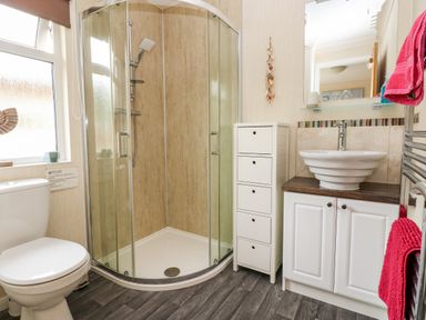 A bathroom with a shower enclosure toilet white cabinet with a washbasin and red towels at 95 The Haven in Wisemans Bridge near Saundersfoot