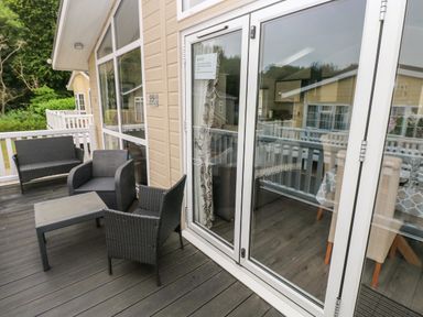An outdoor deck with black wicker chairs and table outside a wooden building with glass doors at 95 The Haven Wisemans Bridge near Saundersfoot