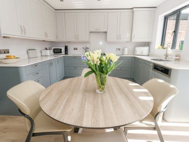 A kitchen with a round wooden table and chairs and a bouquet on the table at Captains Retreat in Christchurch