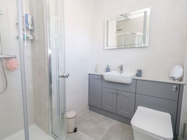A bathroom with a shower enclosure a gray cabinet with a sink mirror and a toilet at Captains Retreat in Christchurch