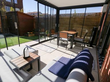 A sunroom with a sofa and a dining table with chairs and a wooden shed outside at Captains Retreat in Christchurch